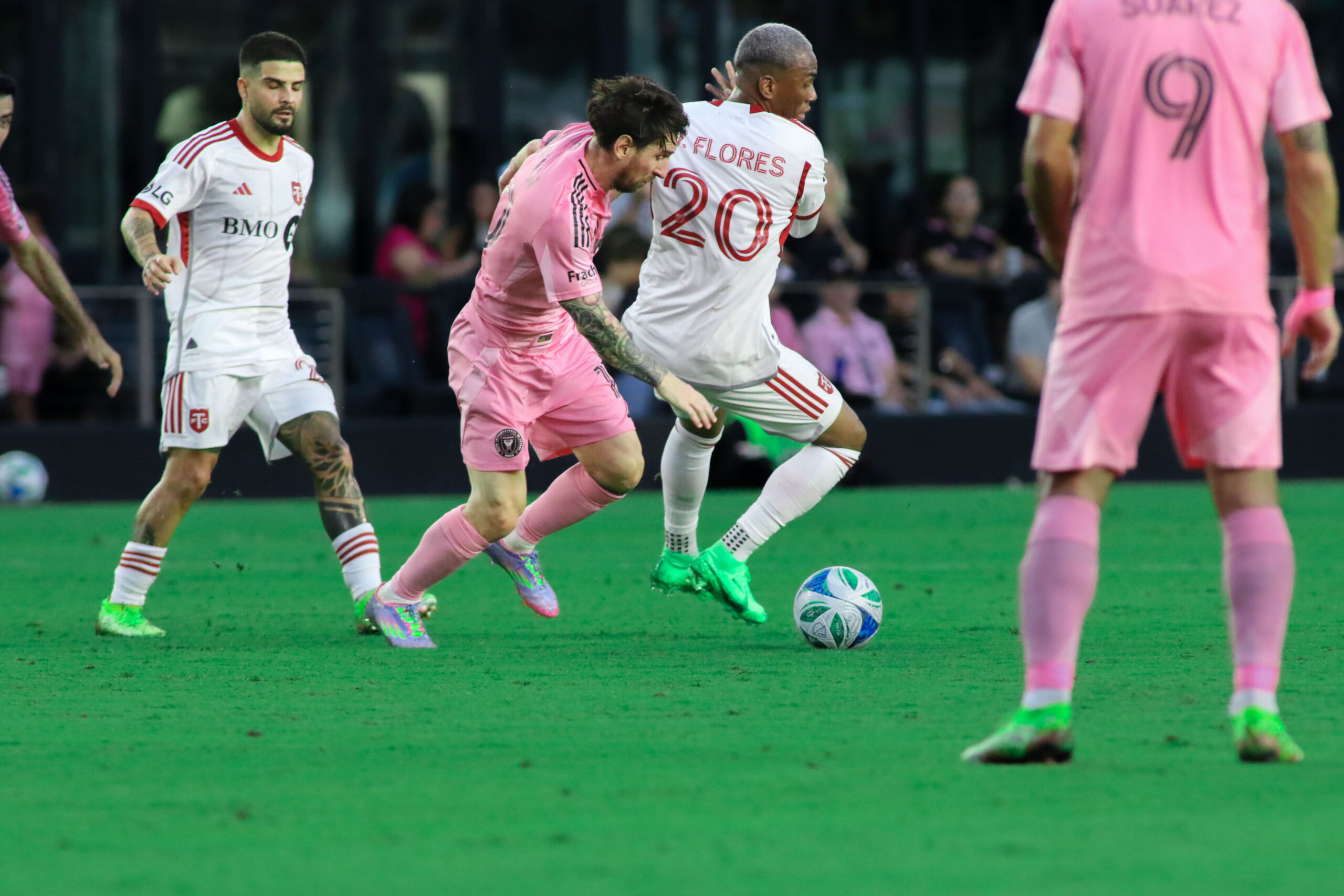 Lionel Messi engages in a spirited duel with Toronto FC’s Deybi Flores as both players fight to recover the ball in a tense midfield moment.